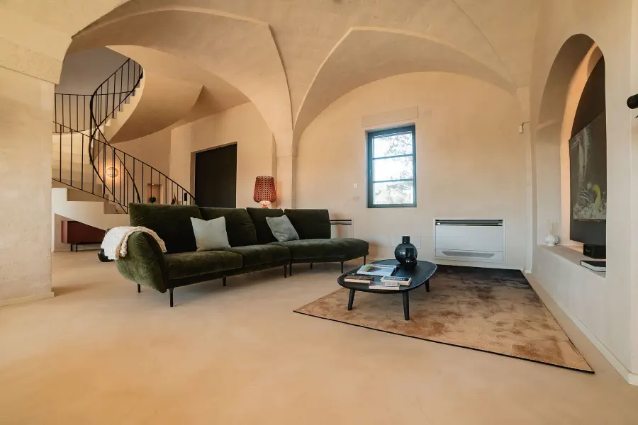 Séjour minimaliste dans un bâtiment en pierre restauré, avec plafond voûté, escalier en colimaçon et mobilier contemporain