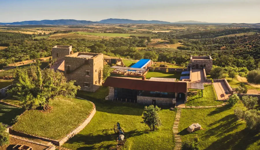 Vue aérienne d’un domaine historique en pierre restauré, avec piscine, entouré d’oliveraies et de collines douces sous une lumière chaude