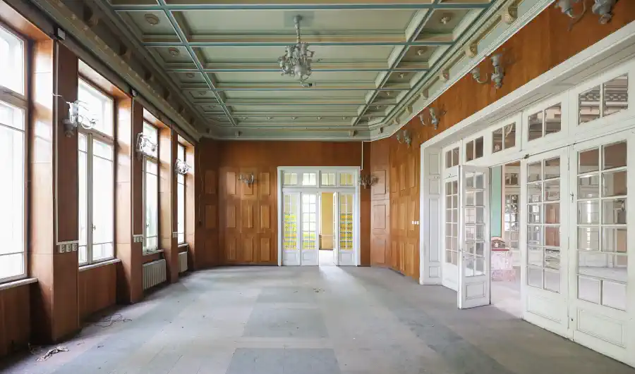 Salle actuellement vide : les boiseries murales fonctionnelles conservées et le plafond à caissons d’origine